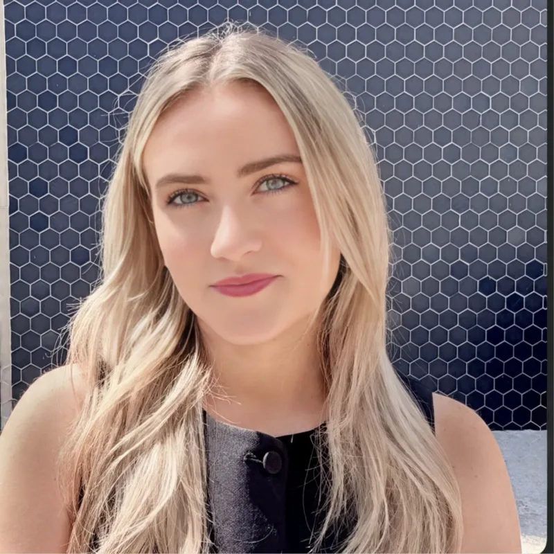 Portrait of Rebeccah, founder of Hyperformant Media, smiling softly against a navy tiled wall